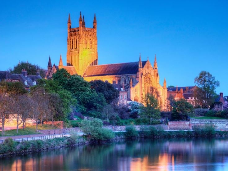 Worcester Cathedral floodlit next to the River Severn at dusk.