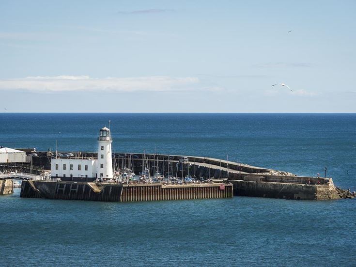 A pier with a white lighthouse surrounded by water.