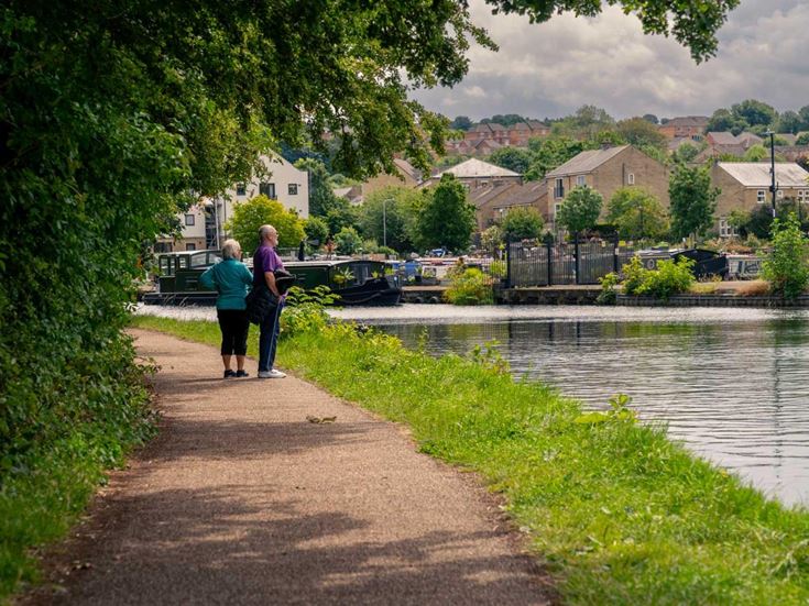 A couple walking along a canal path with a narrow boat in background.