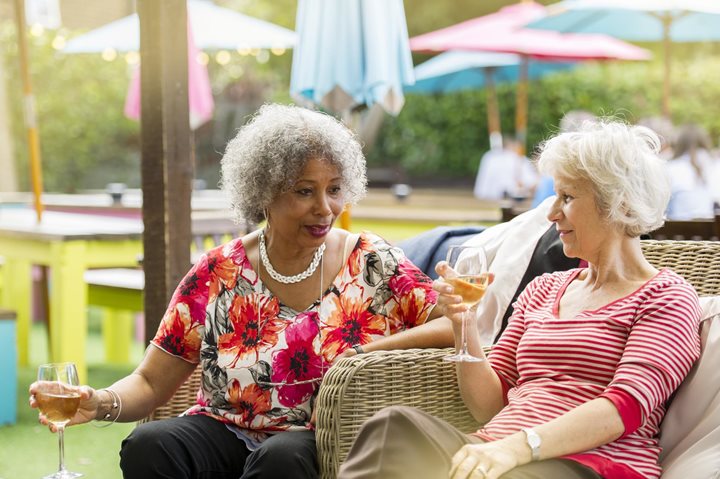 an older woman and an old woman sitting outdoors enjoying a glass of wine