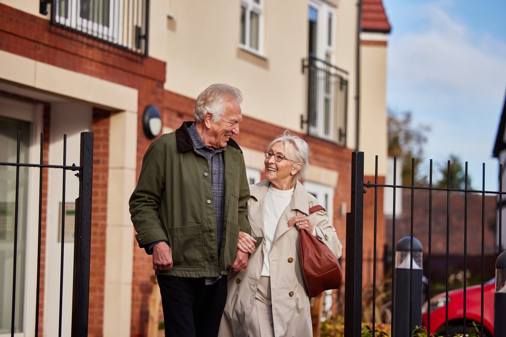 A senior couple walking arm in arm outside a retirement living development