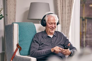 A senior man wearing headphones and looking at his phone