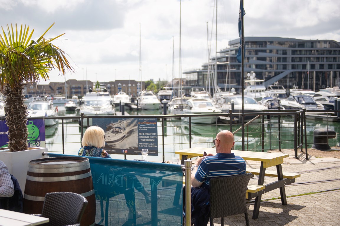 people sitting at a table looking at boats in the water