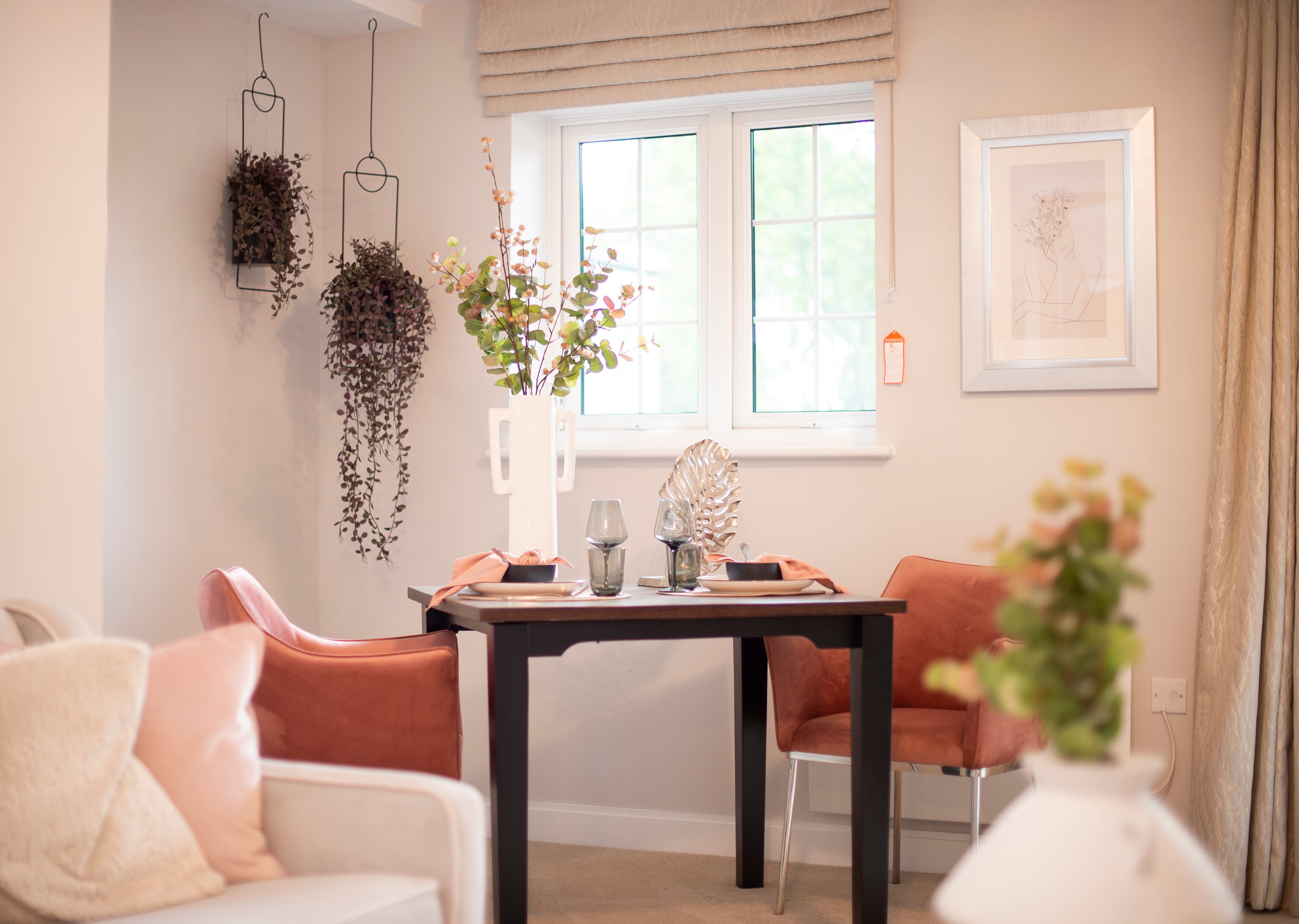 A dining table and chairs positioned by a window in the open-plan living area of a McCarthy Stone retirement home.