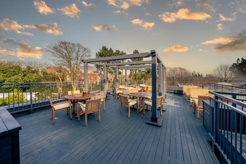 a deck with tables and chairs on it with trees and a sunset in the background
