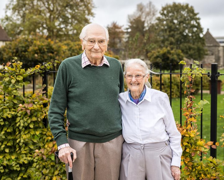 an older couple standing in front of a garden of flowers