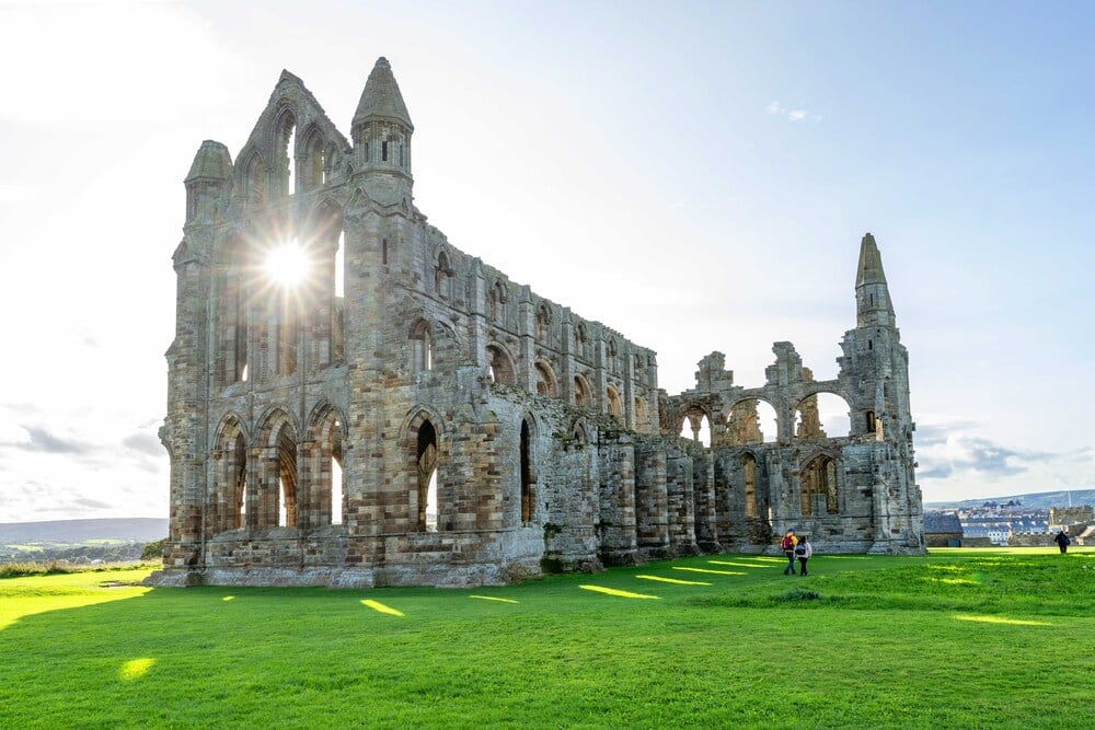 a large stone building with a grass field in front of it with Whitby Abbey in the background