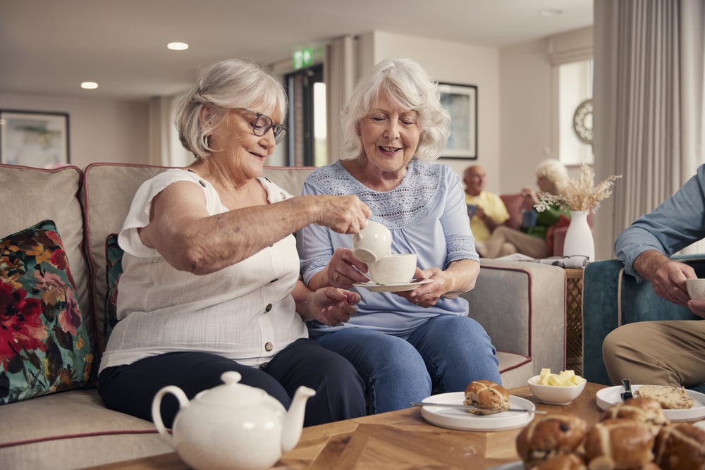 a couple of women sitting on a couch holding tea cups