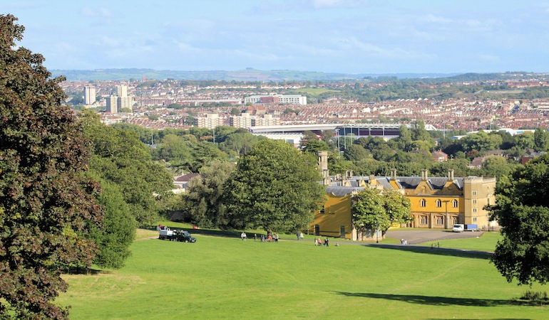 a large green field with buildings and trees in the background