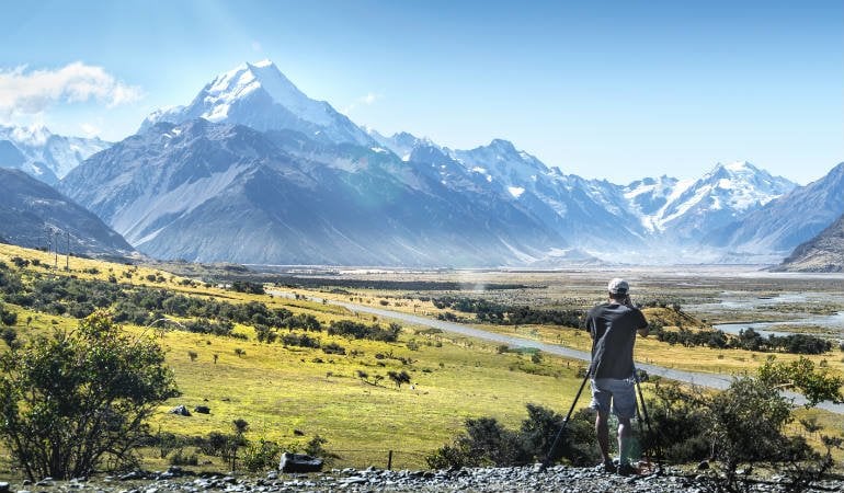 a man standing on a hill with a stick and a mountain in the background