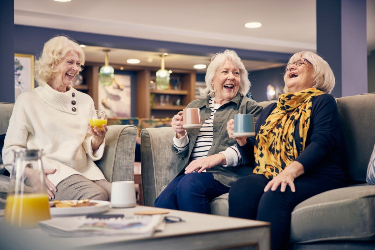 Three women sitting and laughing in the communal area of a McCarthy Stone retirement home