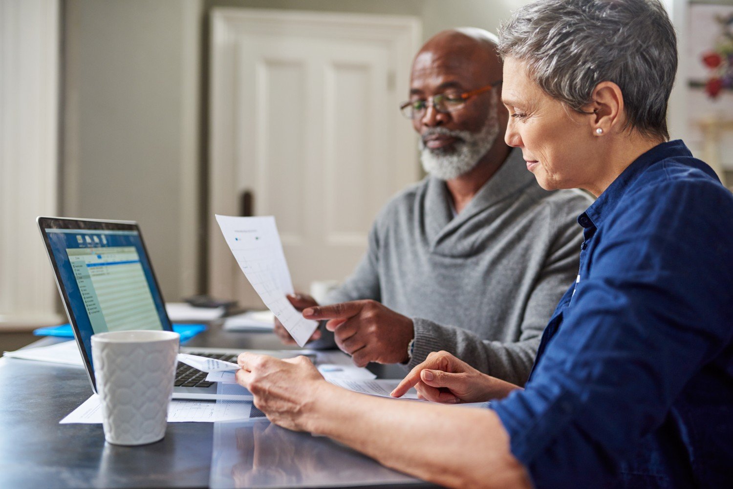 A senior man and woman managing finances with calculator and laptop focusing on pensioners and tax responsibilities