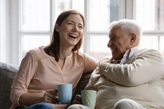 Family members of two generations grown daughter and mature father having fun enjoy tea talk on cozy couch