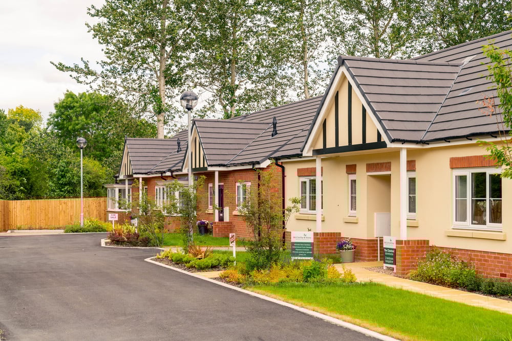 A row of white and red-brick bungalows with tidy front gardens on a quiet street in Quorn