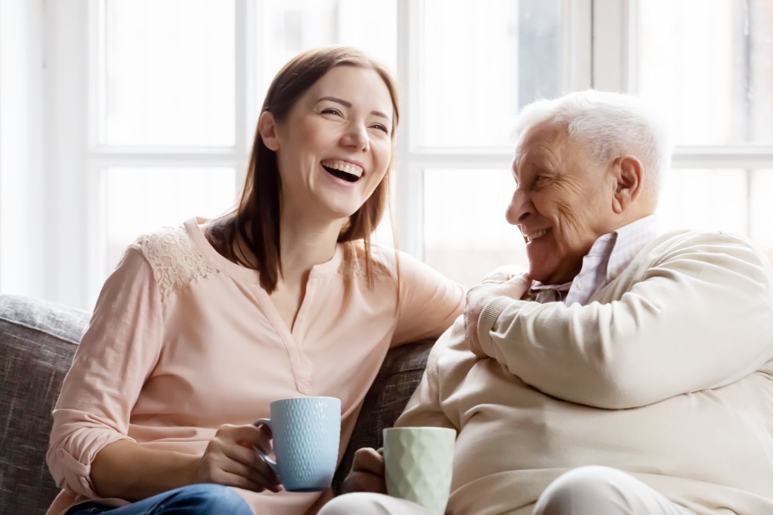 Woman laughing with her elderly father on a sofa, illustrating shared ownership for elderly parents