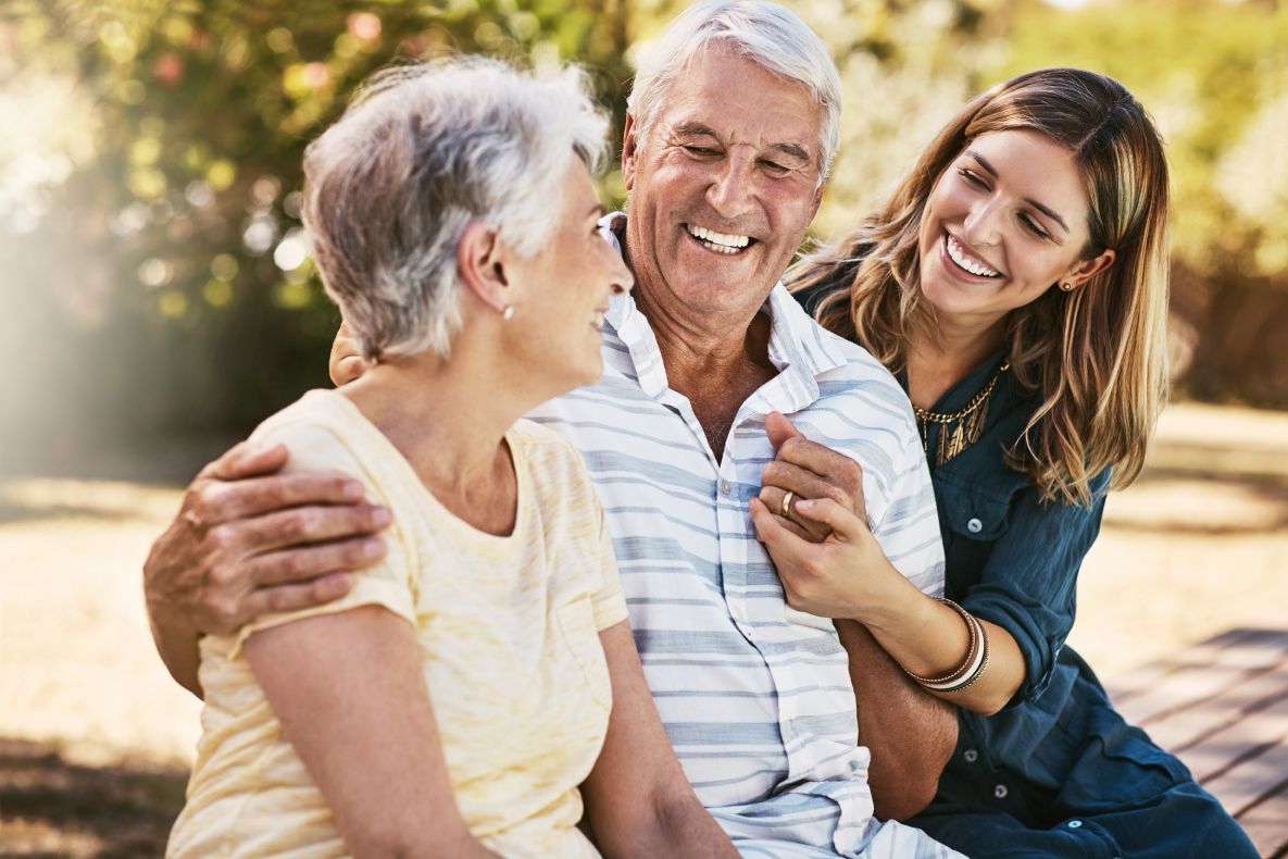 Elderly parents with their daughter, all smiling while sitting outside, showing a family enjoying shared ownership
