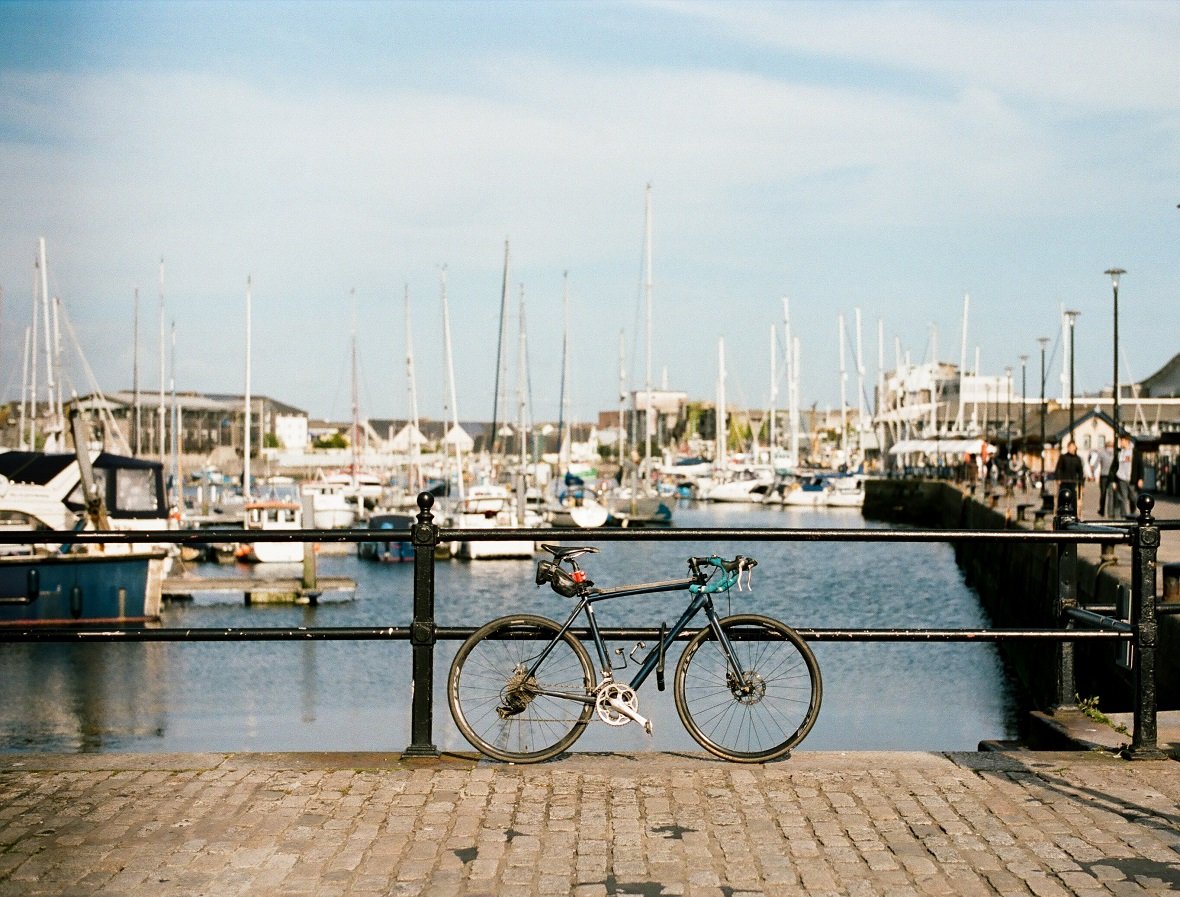 Plymouth marina with numerous boats in the background and a bicycle resting against a railing in the foreground