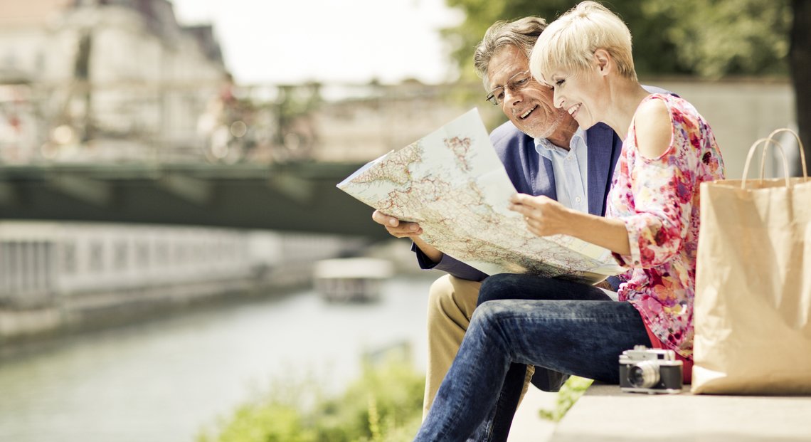 a man and woman sitting on a bench reading a newspaper