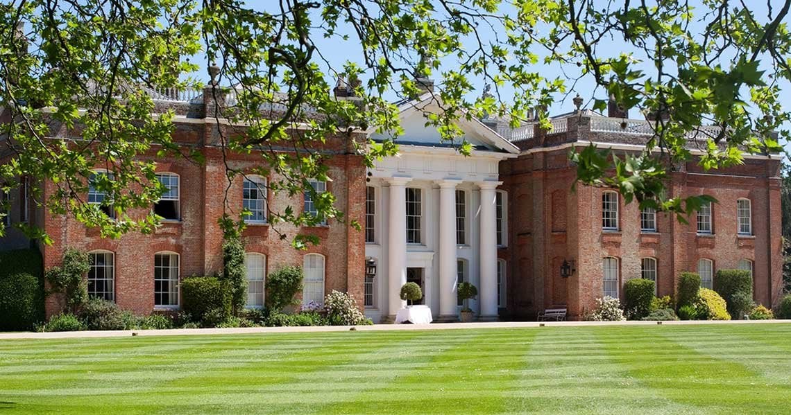 a large brick building with a white column and a green lawn