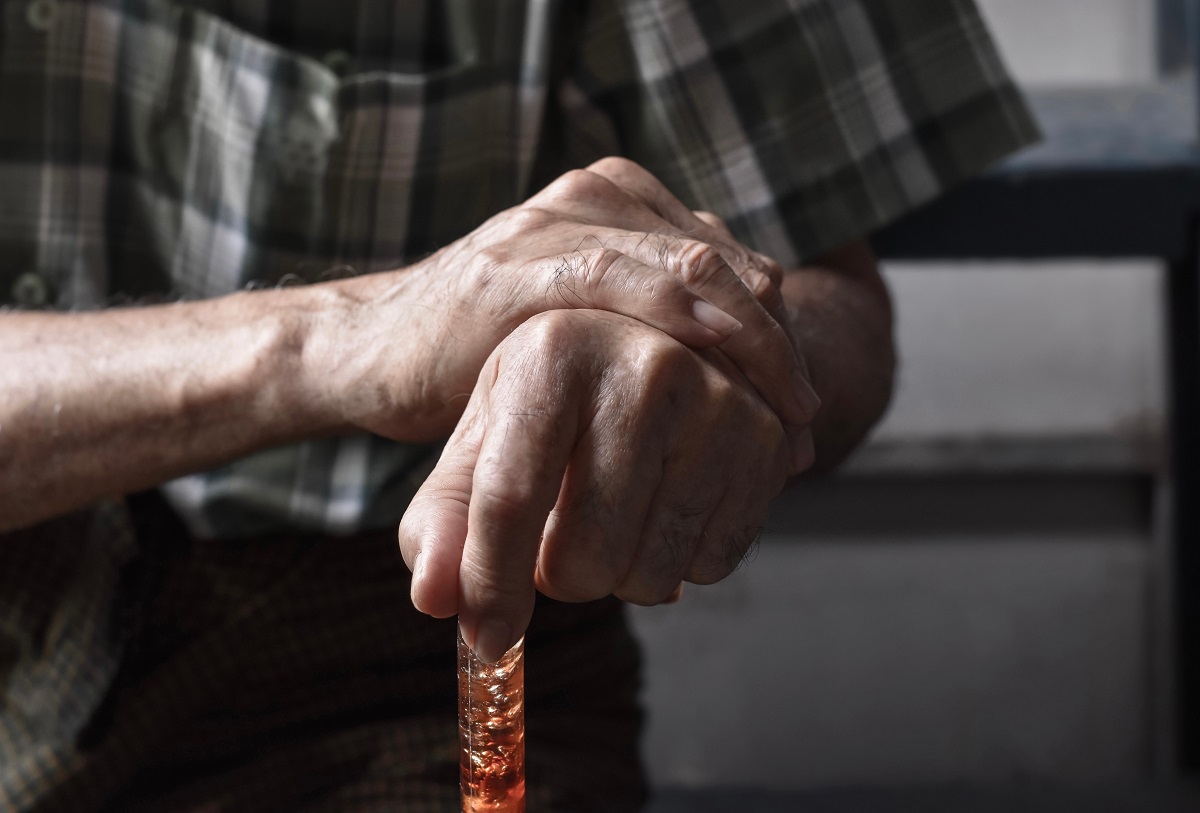 A pair of retiree hands holding a walking stick due to suffering from arthritis.