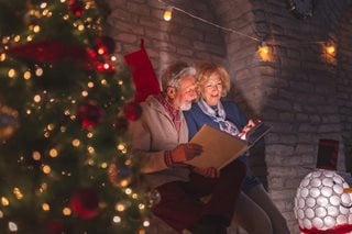 a man and a woman sitting next to a christmas tree looking through photographs