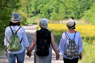Two daughters holdings hands with mother while walking through a park