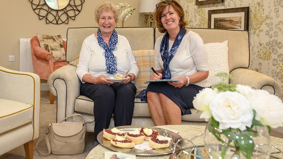 a couple of women sitting on a couch with food and drinks