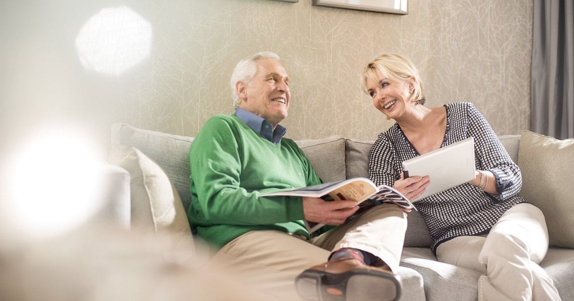 a man and woman sitting on a couch reading a book