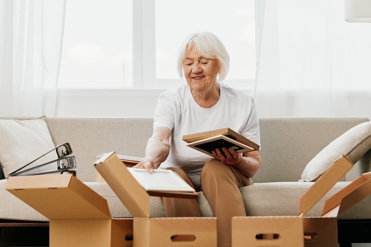 A retiree sitting on a sofa placing items into three boxes