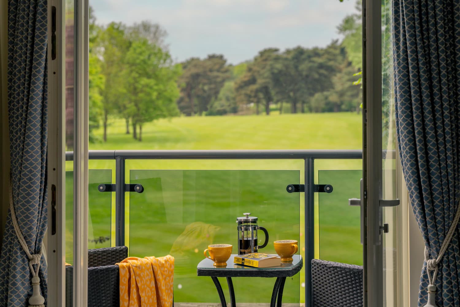 The balcony of a retirement apartment in Bowes Lyon Court, Cheshire. Large doors lead out to the stylish balcony, overlooking a vast green field and trees.