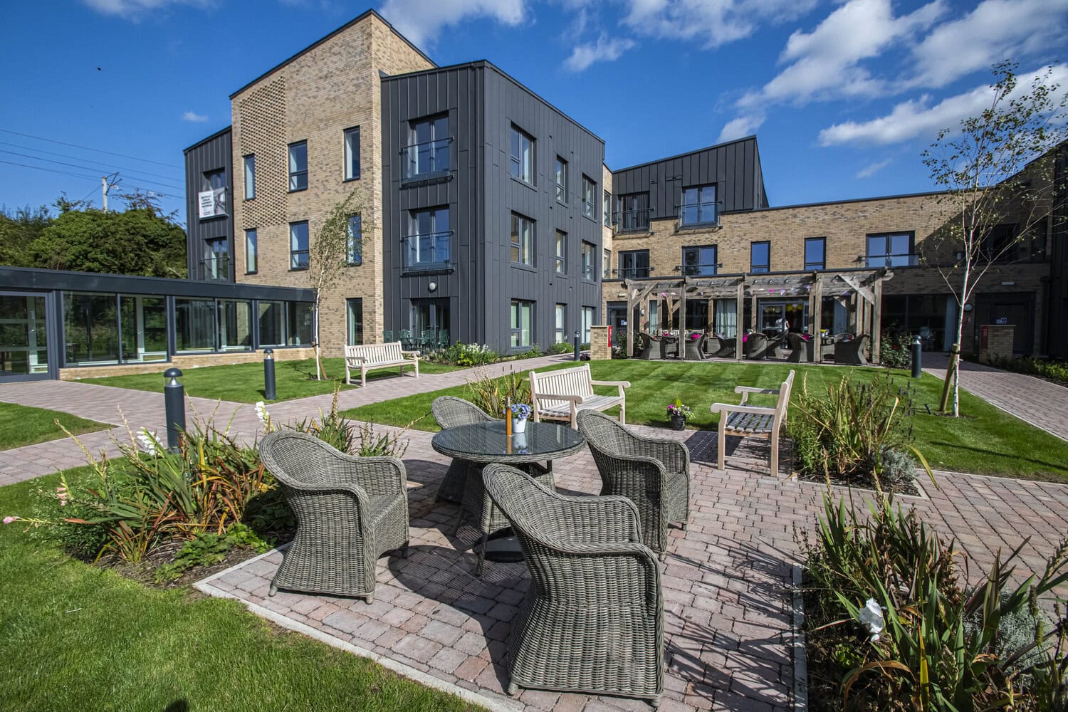 The exterior of a Retirement Living PLUS development in Chipping Norton by McCarthy Stone. The spacious garden, featuring outdoor furniture and plants, is overlooked by beautiful retirement apartments.