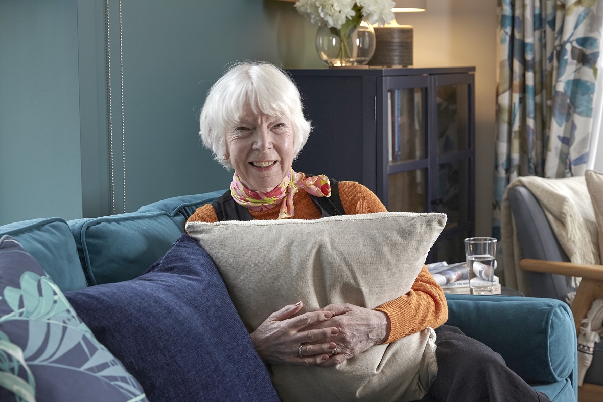 Homeowner Margaret sitting on her blue sofa in her living room, holding a cream cushion and smiling to camera