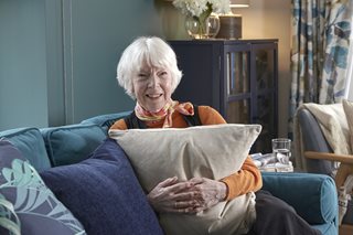 Homeowner Margaret sitting on her blue sofa in her living room, holding a cream cushion and smiling to camera
