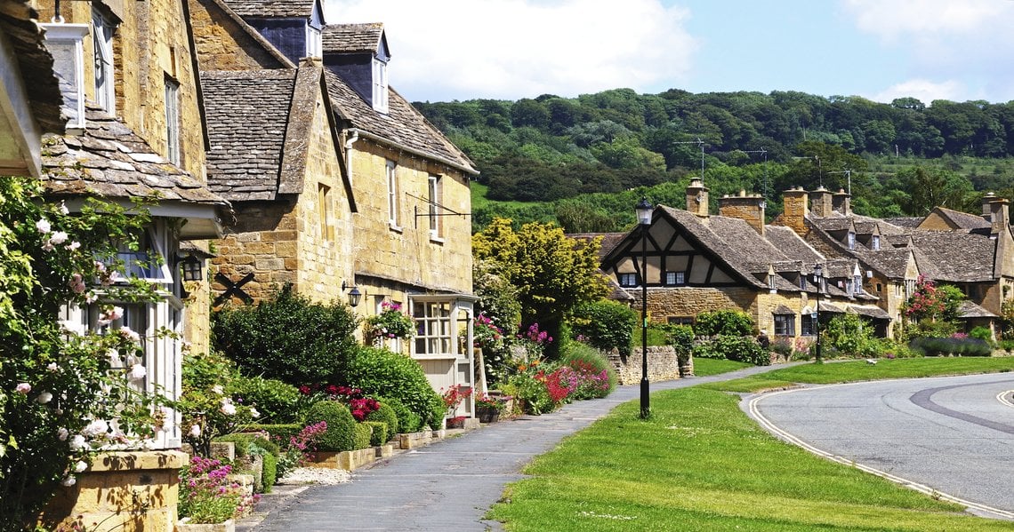 a row of houses with trees in the background with Cotswolds in the background