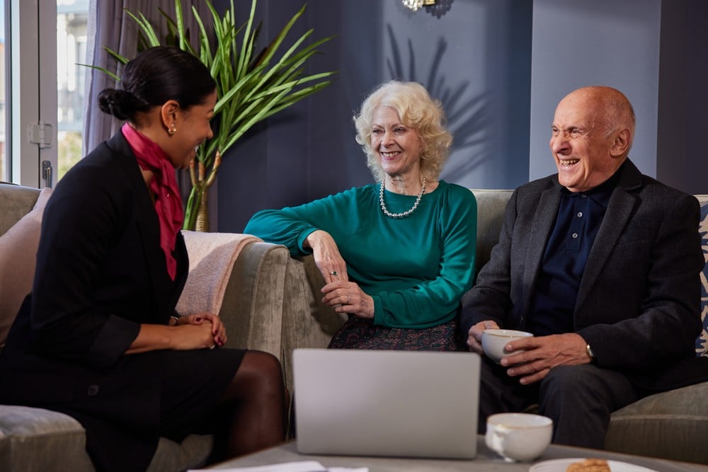 A retired couple sits on the sofa in front of a laptop, in conversation with a McCarthy Stone Sales Consultant