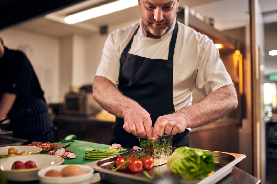 Chef prepping a salad with fresh tomatoes, lettuce and watercress