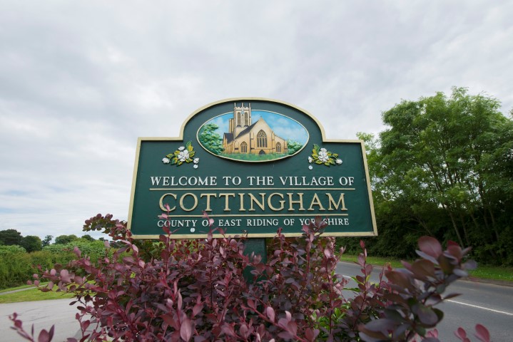 a sign with a flower bed in front of trees