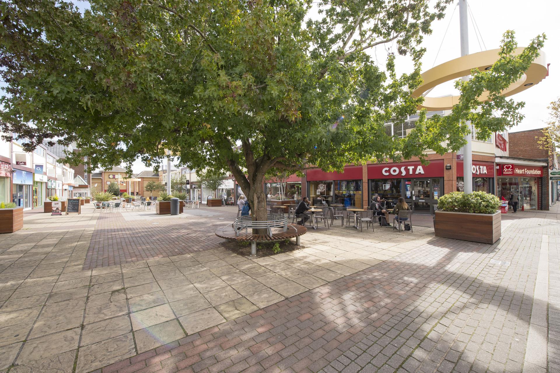 a brick paved area with a tree and benches and a building with a sign on the side