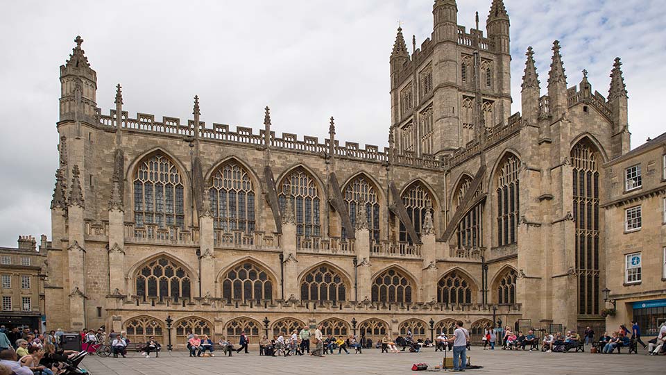 a large stone building with people outside with Bath Abbey in the background