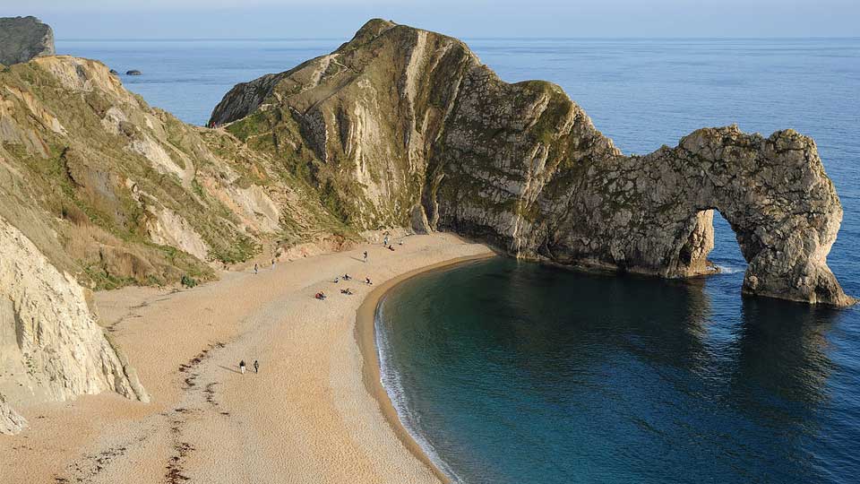 a beach with a large rock formation with Durdle Door in the background