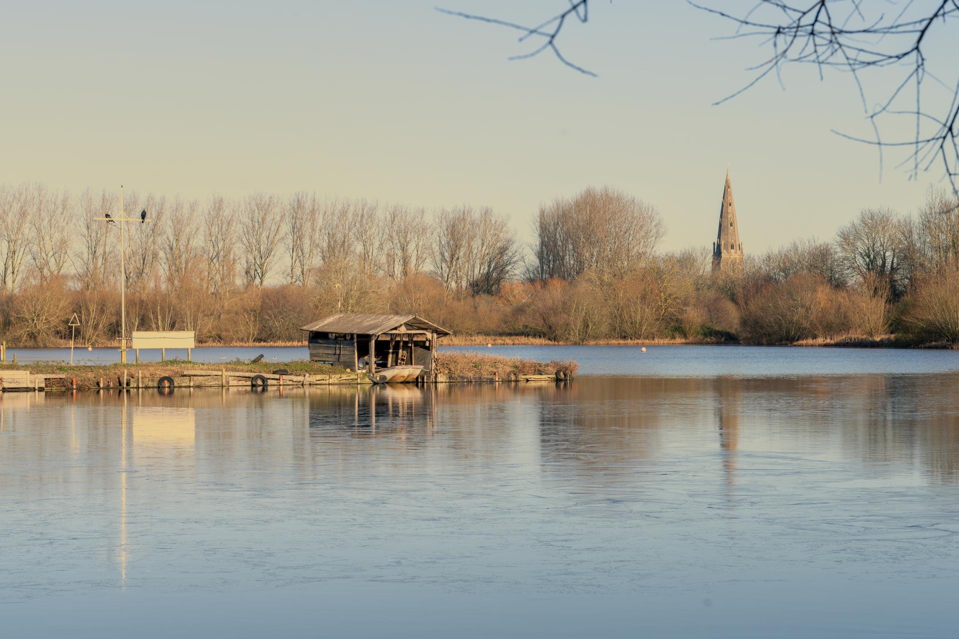 a small building on a dock in a lake with trees and a tower in the background