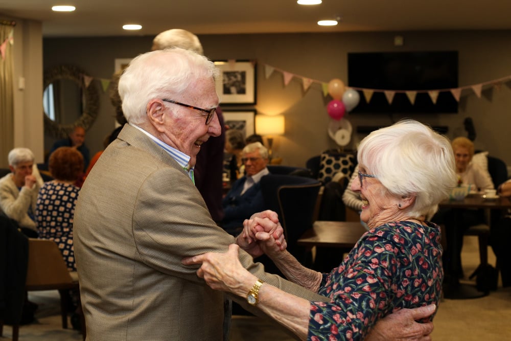 A gathering of retirees smiling laughing and dancing in a communal area