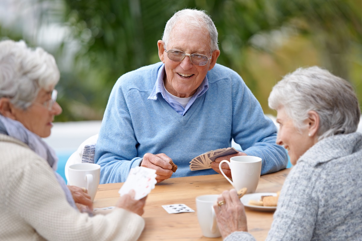 Seniors positioned around a table laughing and joking while playing a card game