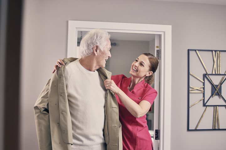 Carer helping an older man put on his coat in a retirement community