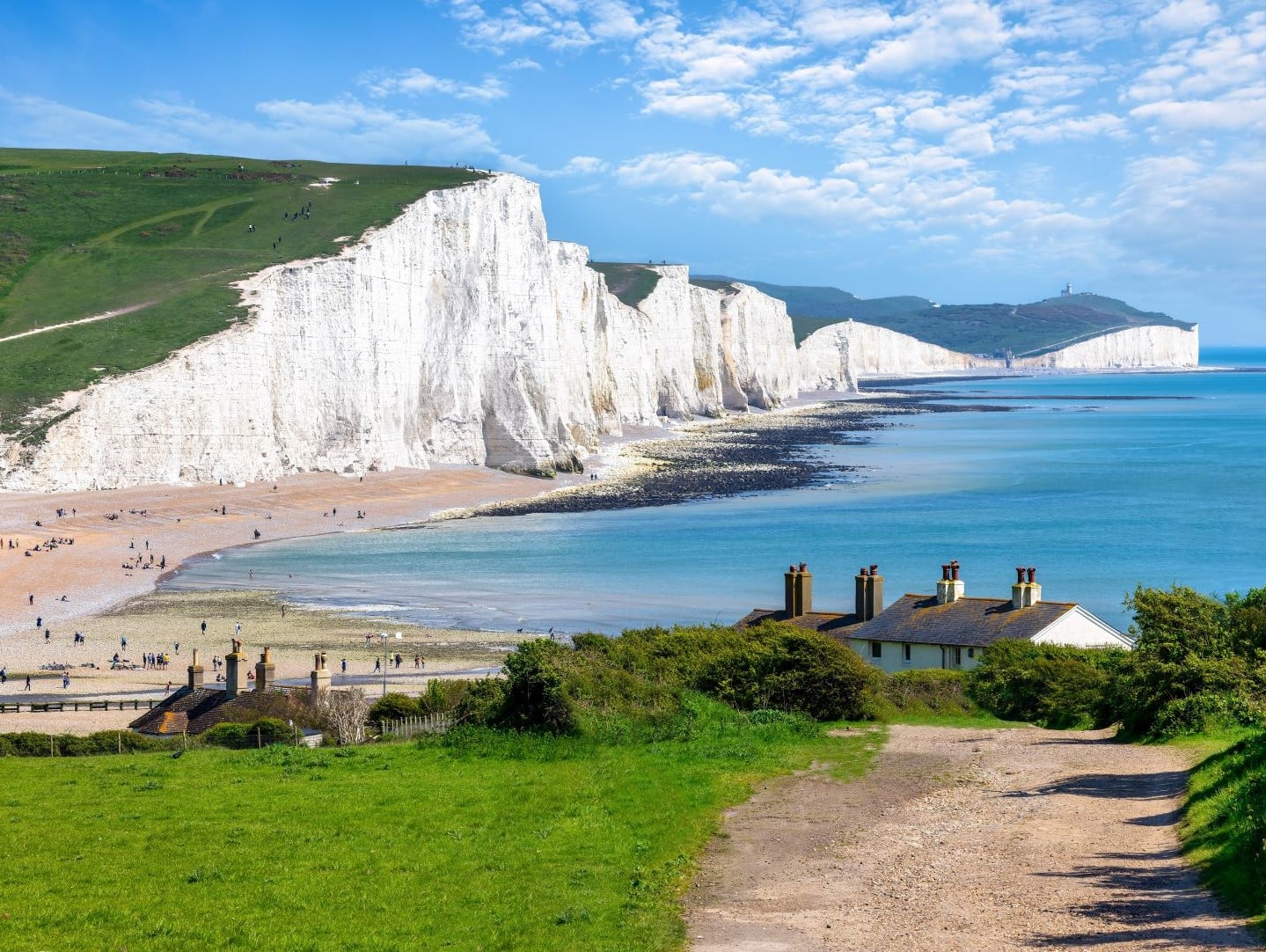 A path leading to buildings and beach with the White Cliffs of Dover in the background.