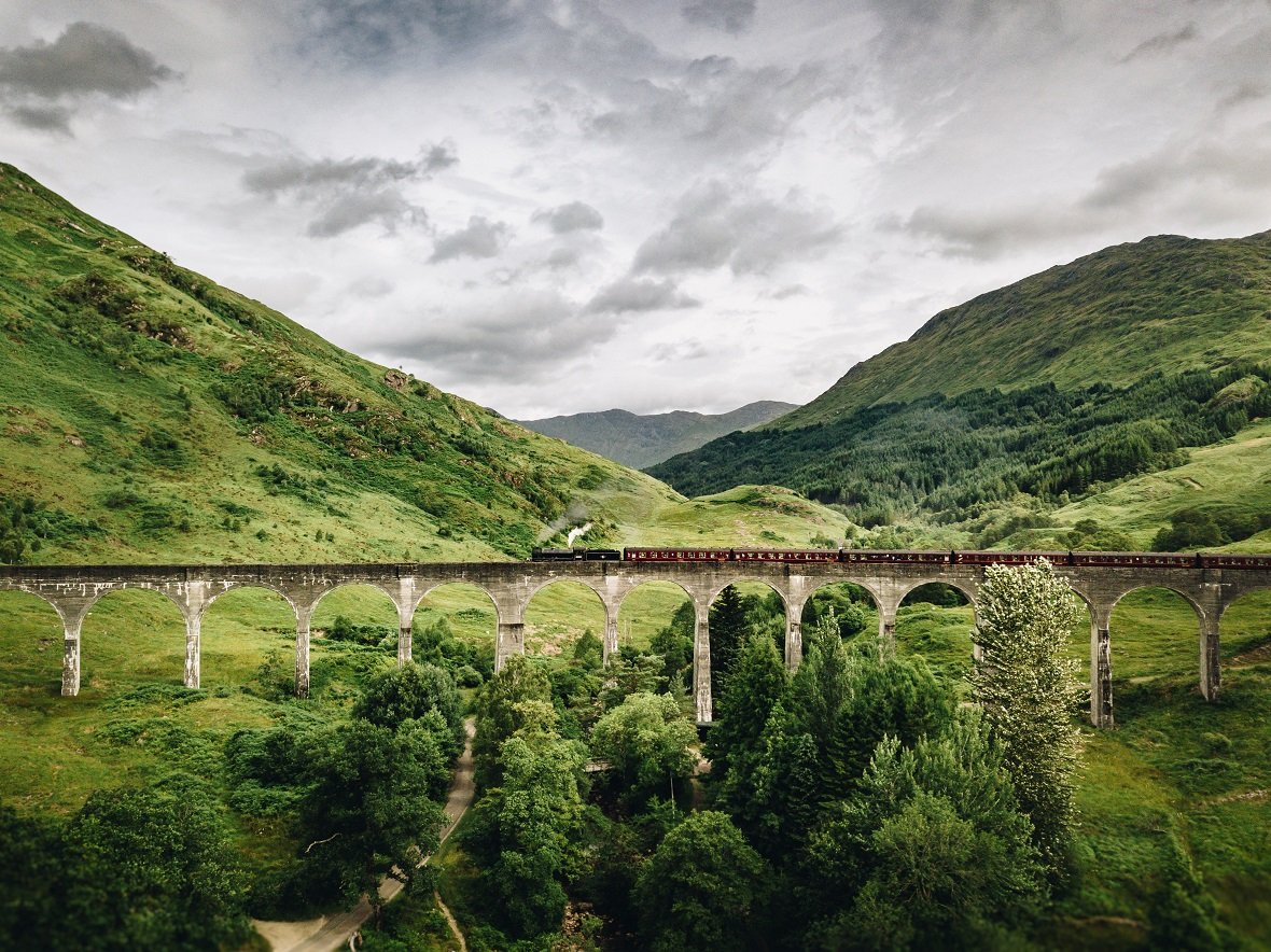 A stone railway bridge with lots of arches in Scotland, with green hills and grey skies behind.