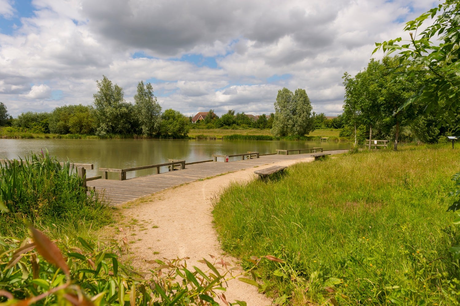 Public seating set among trees and grass overlooking the water in Cambourne.