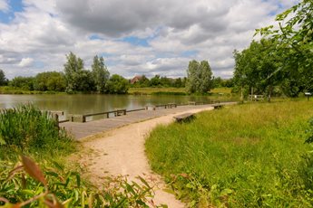 Public seating set among trees and grass overlooking the water in Cambourne.