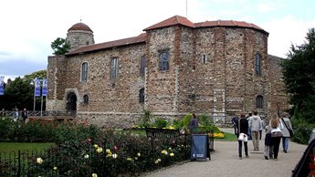 a brick building with a large garden in front of it with Colchester Castle in the background
