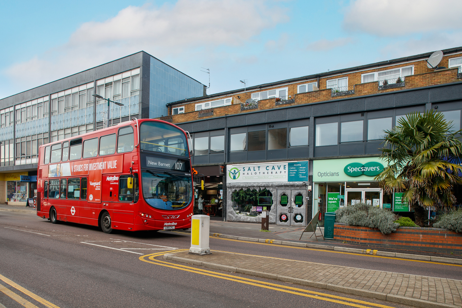 A red double decker bus parked outside local shops on Shenley Road.